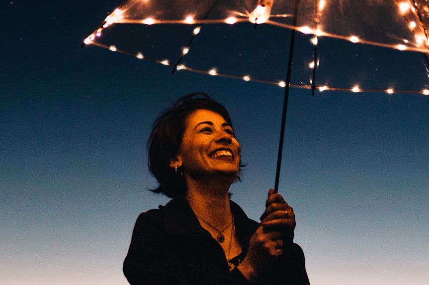 Smiling woman under lit umbrella at night with visible noise before denoise applied