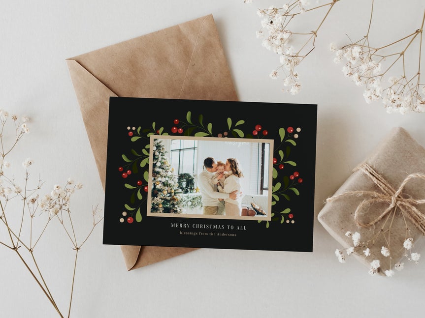 Printed holiday card made with a card maker, featuring a family photo, holly illustration, and gift wrapping props