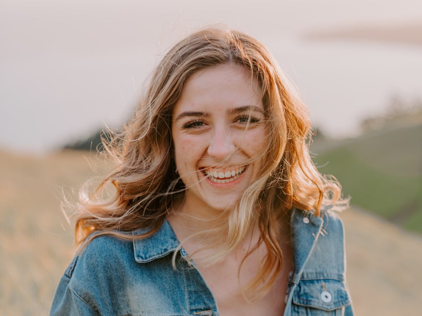 Woman smiling outdoors before using portrait enhancer, with natural lighting and texture