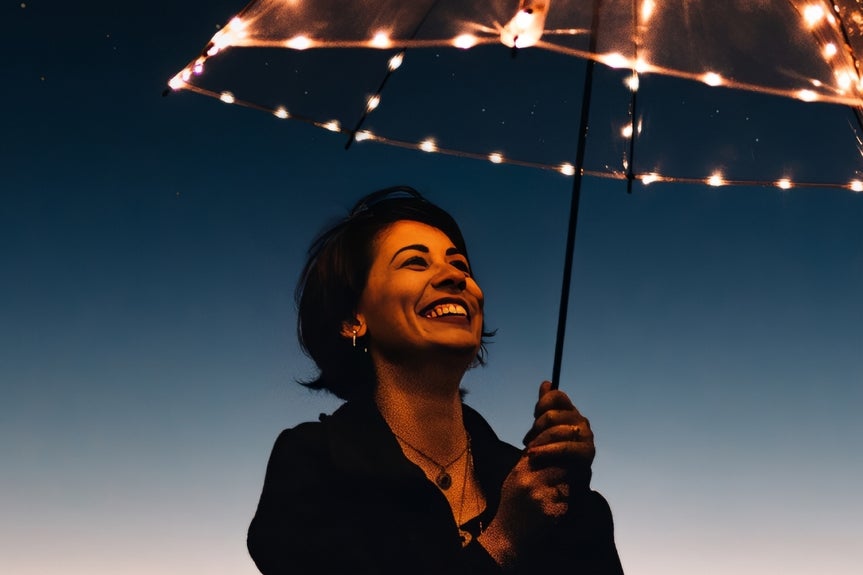 Smiling woman under lit umbrella with night sky, enhanced with denoise for clarity
